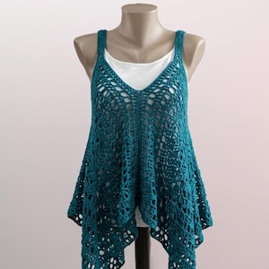 May include: Teal crochet top with a V-neck and wide straps, displayed on a mannequin. The open weave design creates a flowing, asymmetrical hemline. A white vest is visible underneath.