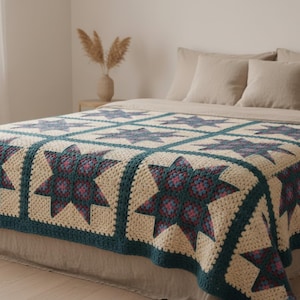 May include: A handmade crochet blanket featuring a repeating star pattern in shades of teal, dark blue, and magenta, framed by cream-colored borders. The textile is constructed from individual square blocks joined together with a dark teal yarn.