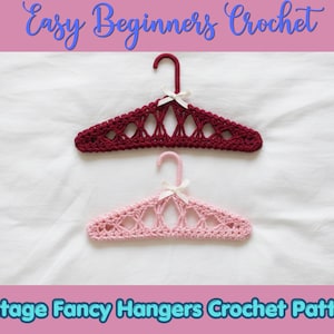 Puede incluir: Dos perchas cubiertas de ganchillo, una de color rojo oscuro y otra de color rosa claro, cada una con un patrón calado decorativo y un pequeño lazo de cinta blanca en el centro. El texto "Easy Beginners Crochet" y "Vintage Fancy Hangers Crochet Pattern" es visible.