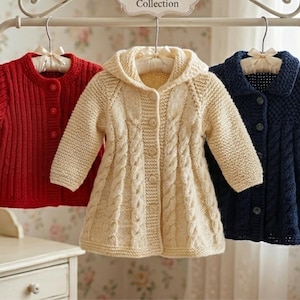 May include: Three knitted children's cardigans in red, cream, and navy blue hang on a white rack. The red cardigan has a ribbed texture, the cream one has a hooded design with a cable knit pattern, and the navy blue one has a collar.