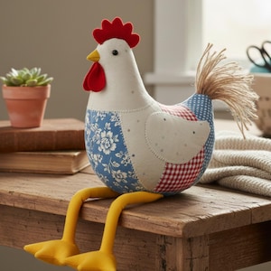 May include: A handcrafted fabric chicken with a red comb and wattle, yellow feet, and a textured tail. The chicken's body features patchwork patterns in blue floral, red gingham, and dotted fabrics. It is sitting on a wooden surface.