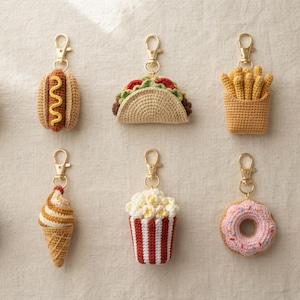 May include: A collection of ten crocheted food keychains featuring a hamburger, hot dog, taco, french fries, pizza slice, sushi roll, soft serve ice cream cone, popcorn bucket, pink frosted doughnut, and a beverage cup, all with gold-tone clasps.