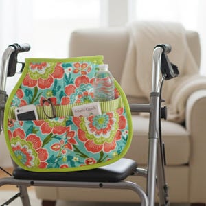 May include: A floral print walker bag with a teal background, red and orange flowers, and a green border. The bag has multiple pockets holding a water bottle, phone, and glasses. The text "Gilbert Oaks" is visible on a small card.