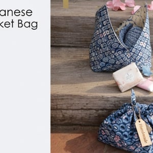 May include: Japanese market bags in a blue and white floral pattern are displayed on wooden steps. One bag is open, revealing a folded interior. A second bag is tied closed with a tag that reads "Handmade". A bar of soap and a tube of lotion are also present.