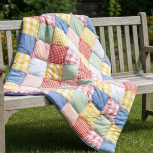 May include: A patchwork quilt featuring a grid of stuffed fabric squares in a gingham pattern. The quilt displays a variety of colors including yellow, blue, green, red, and white, with small fabric knots at the corners of each individual square.