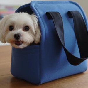May include: A small white dog with dark eyes and a black nose peeking out from a bright blue pet carrier bag. The carrier features a structured rectangular shape with two sturdy black fabric handles attached to the top for easy carrying.