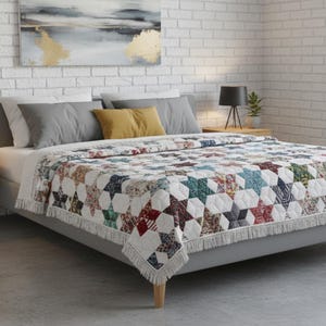 May include: A bed with a gray frame and a colorful star-patterned quilt. The quilt features various colors including red, blue, green, and white. Gray and yellow pillows are on the bed. The quilt has a fringe along the bottom edge. Two nightstands with lamps are on either side of the bed.