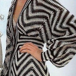May include: A long-sleeved crochet cardigan featuring a bold black and white chevron pattern. The garment has a deep V-neckline, a button-front closure, and voluminous sleeves with fitted cuffs, showcasing intricate yarn work throughout the piece.
