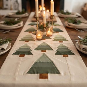 May include: A cream-colored fabric table runner featuring a repeating pattern of stylized Christmas trees. Each tree is constructed from layered horizontal bands of varying shades of green fabric with a small brown square at the base.