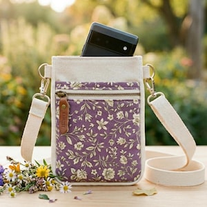 Peut inclure: Un sac bandoulière vertical en toile blanc cassé doté d'une poche avant à motif floral violet. Le sac comprend une fermeture éclair en laiton avec une tirette en cuir marron marquée HARVEST, des ferrures en métal doré et une bandoulière assortie.