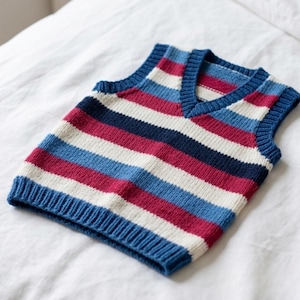 Puede incluir: Un chaleco de punto sin mangas con un patrón de rayas horizontales en tonos azul marino, azul claro, crema y magenta. La prenda presenta un cuello en pico y bordes acanalados en las sisas, el escote y el dobladillo inferior.