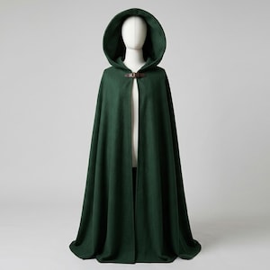 May include: A floor-length dark green hooded cloak featuring a structured hood and a brown leather strap closure at the neck. The garment is displayed on a white mannequin, showcasing a simple, flowing design with a solid, deep green color.