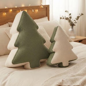 May include: Two tree-shaped throw pillows made of textured sherpa fabric. The larger pillow features a sage green front and cream back, while the smaller pillow has a cream front and sage green back, both with a soft, plush, and fuzzy surface.
