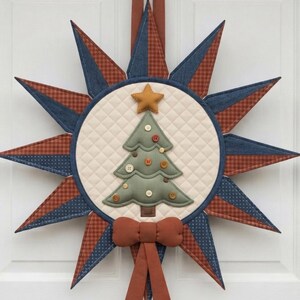Op de afbeelding: Een gewatteerde stoffen wandhanger in de vorm van een ster met twaalf punten. Het midden bevat een crèmekleurige gewatteerde cirkel met een kerstboom van saliegroene stof, versierd met kleine knoopjes en een gouden ster als piek.