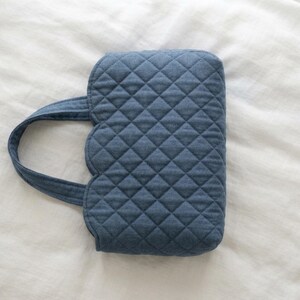 May include: A blue quilted handbag featuring a diamond-stitched pattern and a scalloped edge design. The bag includes a single integrated handle attached to the side, constructed from the same blue fabric with a consistent quilted texture throughout.
