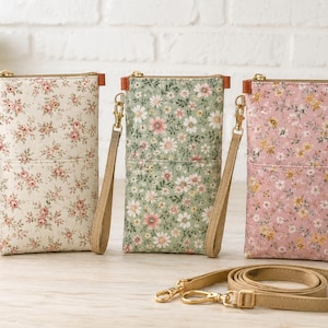 Op de afbeelding: Drie rechthoekige stoffen tasjes met bloemenpatronen in crème, saliegroen en oudroze. Elk tasje is voorzien van een goudkleurige rits, een afneembaar beige polsbandje en een bijpassende verstelbare schouderriem met goudkleurige metalen sluitingen.