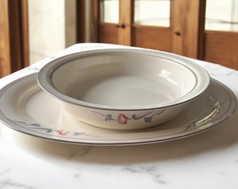 May include: A white ceramic bowl with a floral design and a grey rim, nested inside a larger white ceramic plate with a similar floral design and grey rim.