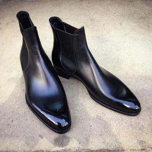May include: A pair of black leather Chelsea boots. The boots have a sleek, polished appearance with a pointed toe and elastic side panels. The boots are designed for a classic, sophisticated look.