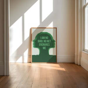 May include: A framed art print featuring a green silhouette of a tree-like figure with the text "I AM NO BIRD; NO NET ENSNARES ME." The artwork is set against a light background, with a wooden frame. The print is displayed on a wooden floor.