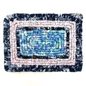 May include: A rectangular, handmade rag rug with a multi-colored design. The rug features a dark blue border, a pink floral pattern, and a blue and green center. The rug is made of fabric strips woven together.