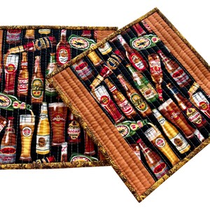 May include: Two brown quilted pot holders with a black background and a pattern of various beer bottles and glasses. The pot holders have gold trim.