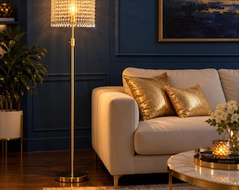 May include: A tall floor lamp with a slender gold-toned metal stand and a circular base. The cylindrical lampshade is constructed from numerous hanging clear glass crystals that diffuse the warm light from the central bulb.