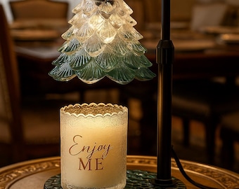 May include: A decorative lamp with a green and clear glass shade shaped like a Christmas tree. A candle with the words "Enjoy ME" is on a green base. The lamp has a black metal frame and sits on a gold-colored table.