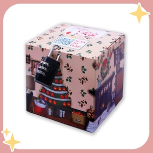 Könnte beinhalten: Eine würfelförmige Geschenkbox mit einem schwarzen Zahlenschloss. Die Box hat ein weihnachtliches Design mit einem geschmückten Baum, einem Kamin und Stechpalmen. Auf der Box steht "Scan to Play!" und "Christmas Fest".