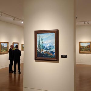 以下が含まれることがあります： 木製の額縁に入った風景画が展示されているアートギャラリー。中央の絵画は、青と白の色合いの山の風景を描いています。スーツを着た2人が、そのアートワークを鑑賞しています。