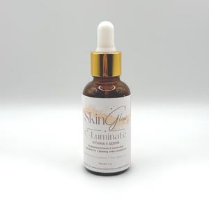 May include: A brown glass bottle with a gold lid and dropper top. The bottle is labeled "Skin Glow Luminate Vitamin C Serum" and says "Brightening Vitamin C serum that works for a glowing, even complexion".