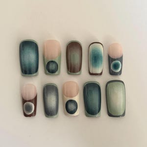 May include: A collection of ten press-on nails with a contemporary design. Each nail showcases a base colour of teal, brown, or green, with a contrasting nude or white tip. Some nails have a dark circle accent. The nails are rectangular in shape.
