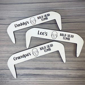 Könnte beinhalten: Drei Holzkämme mit einzigartigem Design, jeweils mit einem Namen und dem Schriftzug "Bald Head Comb". Die Namen sind "Daddy's", "Lee's" und "Grandpa's", mit einer einfachen Glatzkopf-Illustration.
