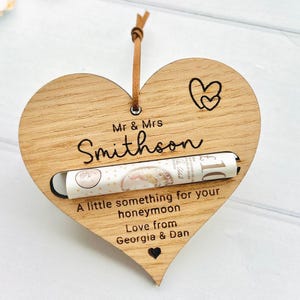 Può includere: Regalo a forma di cuore in legno con fessura per soldi, con i nomi "Mr & Mrs Smithson". Il cuore ha un cordino in pelle per appenderlo e il testo "A little something for your honeymoon, Love from Georgia & Dan."