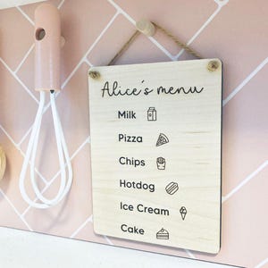 May include: Wooden sign with the text "Alice's menu" and food icons. The menu includes milk, pizza, chips, hotdog, ice cream, and cake. Kitchen utensils hang on the left side of the image.