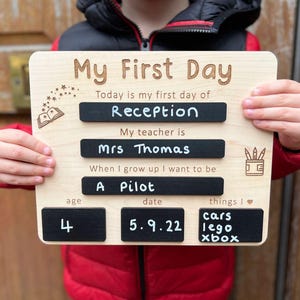 May include: A wooden sign with the words "My First Day" and details about a child's first day of school, including "Reception", "Mrs Thomas", and "A Pilot". The sign also shows the child's age, date, and favourite things.