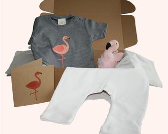 May include: A baby gift set in a cardboard box. The set includes a gray and white striped short-sleeved shirt with a pink flamingo graphic, white pants, a pink plush flamingo toy, and a greeting card with a flamingo illustration.