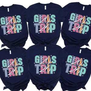 six navy blue t-shirts with the text "GIRLS TRIP" printed on them in a colorful, stylized font.