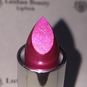 Op de afbeelding: Close-up van een roze lipstick met een glinsterende afwerking. De lipstick zit in een zilveren buis.