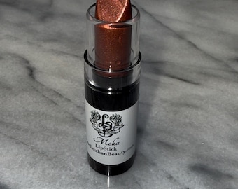 May include: A tube of Moka lipstick with a metallic, reddish-brown hue. The lipstick is encased in a clear plastic tube with a black base and a white label featuring the brand name and website. The lipstick is partially extended.