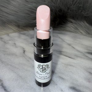May include: A pink lipstick tube with a black label that reads "Blanc Perle Lipstick www.LuxhanBeauty.com".