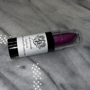 May include: A purple glitter lipstick in a black and white tube with the text "Lavande Lipstick" and "luxthanBeauty.com".