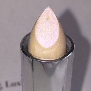 May include: A close-up of a white lip balm with a silver tube. The balm is in a bullet shape and has a pearlescent finish.