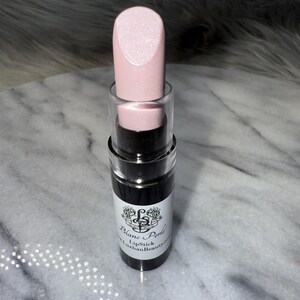 May include: A pink lipstick tube with a black label that reads "Blanc Perle Lipstick LuxhanBeauty.com".