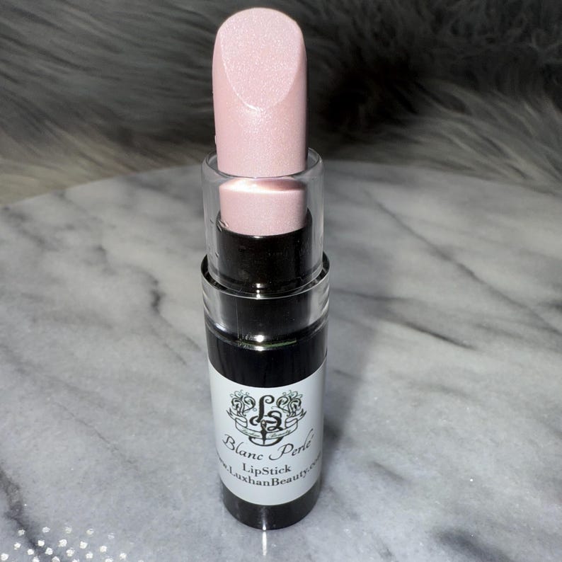 May include: A pink lipstick tube with a clear cap and a black label that reads "Blanc & Perle Lipstick LuxhanBeauty.com".