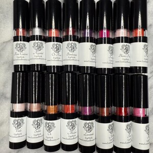 May include: A collection of twenty lipstick tubes, each containing a different shade of lipstick. The tubes are black with a clear window to show the colour of the lipstick. Each tube has a white label with the name of the lipstick colour and the website address "www.LuxhanBeauty.com".