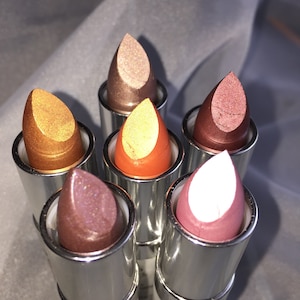 May include: Six silver lipstick tubes with different colored metallic lipsticks. The lipsticks are in shades of gold, copper, bronze, pink, and white.
