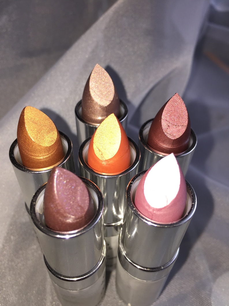 May include: Six silver lipstick tubes with different colored metallic lipsticks. The lipsticks are in shades of gold, copper, bronze, pink, and white.