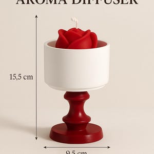 Peut inclure: Un diffuseur d'arômes en forme de rose rouge, placé dans un bol en céramique blanche sur un piédestal en bois rouge. Le diffuseur mesure 15,5 cm de haut et 9,5 cm de large. Il pèse 0,51 kg. Diffuseur d'arômes à base de plantes.