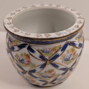 May include: A round porcelain planter featuring a white base with a blue lattice pattern and gold trim. The exterior is decorated with small, colorful floral clusters in shades of pink, blue, and green. The rim has a repeating gold floral motif.