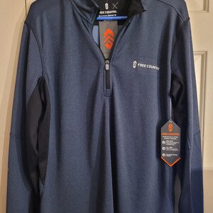 May include: Navy blue long-sleeve pullover with a quarter-zip closure and a black collar. The shirt has black side panels and a tag with the brand name "FREE COUNTRY". The tag has an orange and white design.